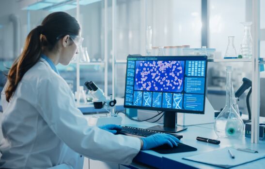 Labor mit modernen technologischen Geräten Medizinisch-wissenschaftliches Labor mit einem multiethnischen Team von Biotechnologie-Wissenschaftlern, die Medikamente entwickeln, und einem Mikrobiologen, der an einem Computer mit einem Display arbeitet, das die Schnittstelle zur Genbearbeitung zeigt.