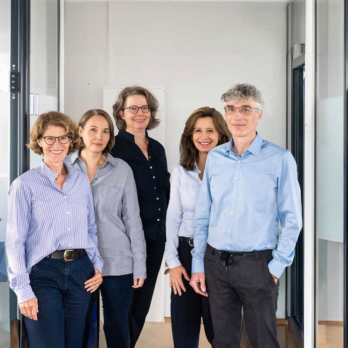 Das Pathologen-Team aus sechs Ärzten steht in Dreier-Reihe leicht versetzt hintereinander in einem Flur. Im Hintergrund Glastüren der modernen Büroräume.