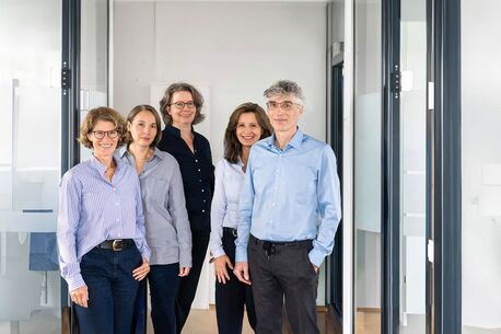 Gruppenfoto: Das Pathologen-Team vor einer weißen Wand. Zwei Frauen sitzen auf einem Stuhl dahinter stehend fünf weitere Pathologen.