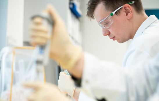 Arbeiten unter Qualitätsmanagement-Standards Mann in weißem Laborkittel und Schutzbrille arbeitet mit einer Pipette konzentriert im Labor.