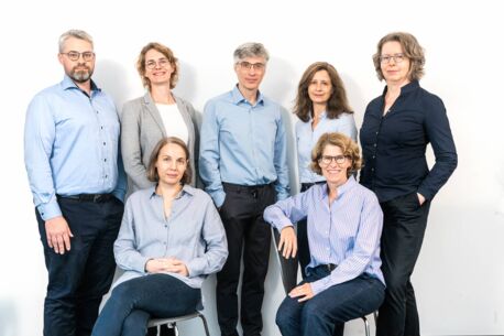Gruppenfoto: Das Pathologen-Team vor einer weißen Wand. Zwei Frauen sitzen auf einem Stuhl dahinter stehend fünf weitere Pathologen.