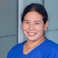 Hämatopathologie Lübeck - Dr. Veronica Bernard Dies ist ein Porträtfoto von Dr. Veronica Bernard. Sie trägt blaue Laborkleidung und blickt lächelnd in die Kamera. Ihre dunklen Haare sind zu einem Zopf gebunden.