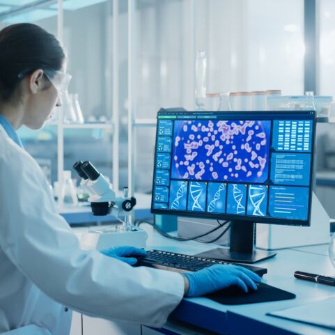 Medizinisch-wissenschaftliches Labor mit einem multiethnischen Team von Biotechnologie-Wissenschaftlern, die Medikamente entwickeln, und einem Mikrobiologen, der an einem Computer mit einem Display arbeitet, das die Schnittstelle zur Genbearbeitung zeigt.