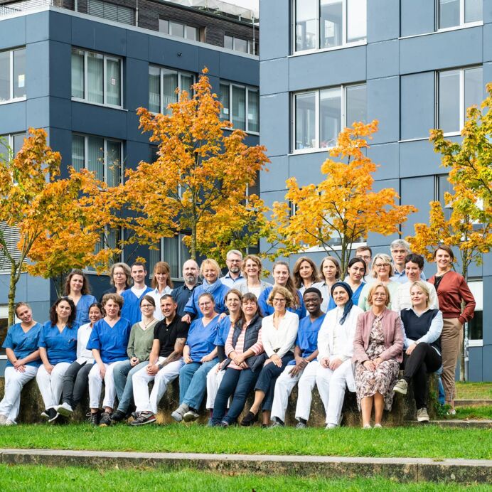 Team Hämatopathologie Lübeck Hämatopathologie Lübeck - Das gesamte Team befindet sich draußen auf einer grünen Wiese. Ein Gruppenfoto aus zwei Reihen. Die erste Reihe sitzt auf einer Steinmauer, die anderen Mitarbeiter stehen dahinter.