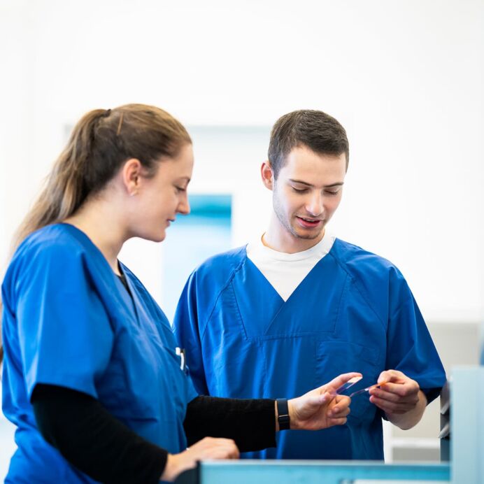 Ausbildung eines Biologielaboranten Zwei Laboranten in blauer Arbeitskleidung diskutieren über eine Probe in einem hellen Laborraum.