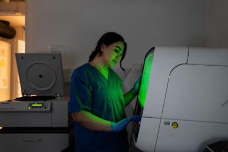 Laborantin in blauer Arbeitskleidung arbeitet mit einem Analysegerät zur NGS-Sequenzierung, das ein grünes Licht ausstrahlt, in einem modernen Labor.