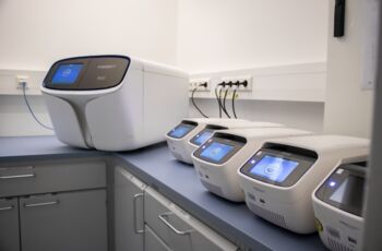 Auf der geräumigen Arbeitsfläche des Labors sind mehrere gleiche Geräte zur Untersuchung von Proben aufgebaut. Ein großes Gerät links, daneben fünf kleine.