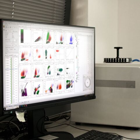 Auf dem Foto ist ein Labor zu sehen, in dem moderne Technologie eingesetzt wird. Ein Computer steht links auf einen Schreibtisch.