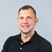 Porträt eines Teamleiters der Hämatopathologie Lübeck in einem schwarzen Polohemd mit tätowiertem Arm vor neutralem Hintergrund.