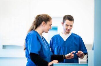 Zwei Laboranten in blauer Arbeitskleidung diskutieren über eine Probe in einem hellen Laborraum.