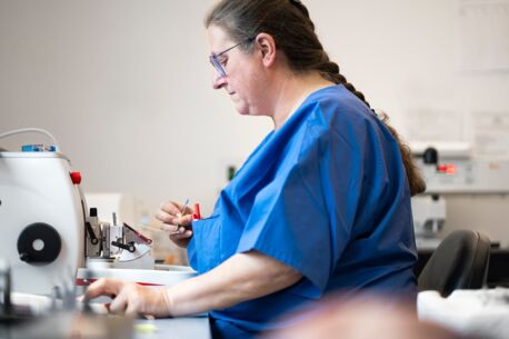 Laborantin in blauer Arbeitskleidung arbeitet konzentriert mit einem Mikrotom, um feine Gewebeschnitte für die Analyse vorzubereiten.