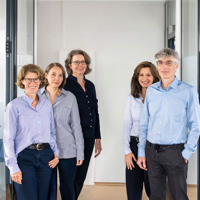 Das Pathologen-Team aus sechs Ärzten steht in Dreier-Reihe leicht versetzt hintereinander in einem Flur. Im Hintergrund Glastüren der modernen Büroräume.