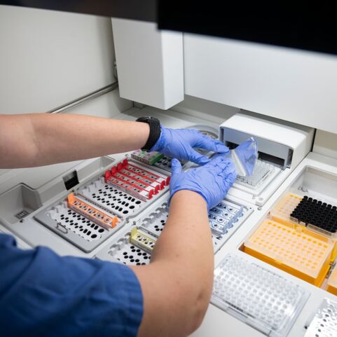 Bestücken des NGS-Sequenzierers Laborant in blauen Handschuhen, der Proben in eine Analysemaschine einfüllt, umgeben von verschiedenen Probenbehältern.